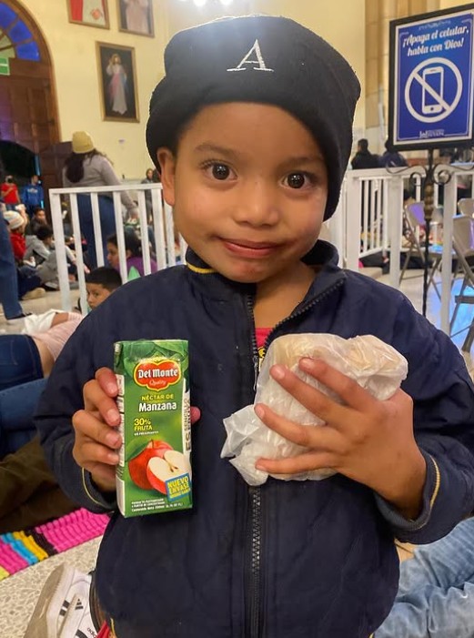 Niño sonriente muestra el jugo y el sándwich que recibió en una jornada de PANAH